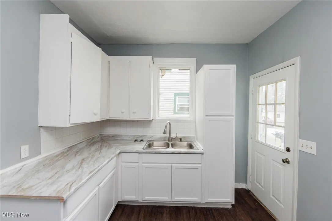 Kitchen featuring white cabinets, decorative backsplash, light countertops, and dark wood-type flooring