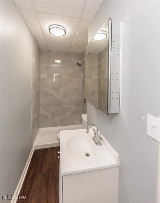 Bathroom with a tile shower, vanity, a drop ceiling, and wood finished floors