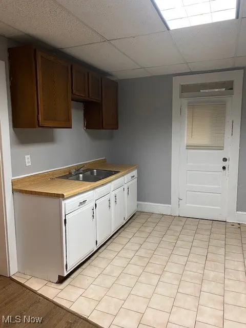Kitchen featuring a paneled ceiling, white cabinets, and light wood-style floors