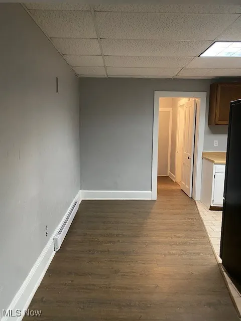 Unfurnished room featuring a baseboard heating unit, a paneled ceiling, and wood finished floors