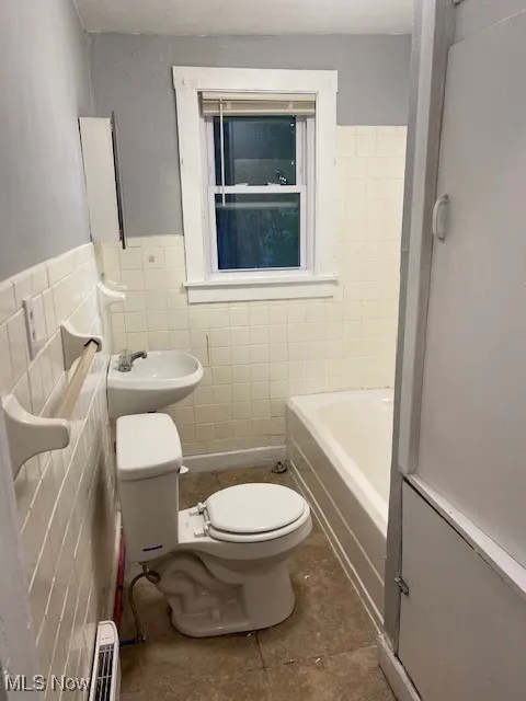 Bathroom with tile walls, a tub to relax in, wainscoting, and a shower