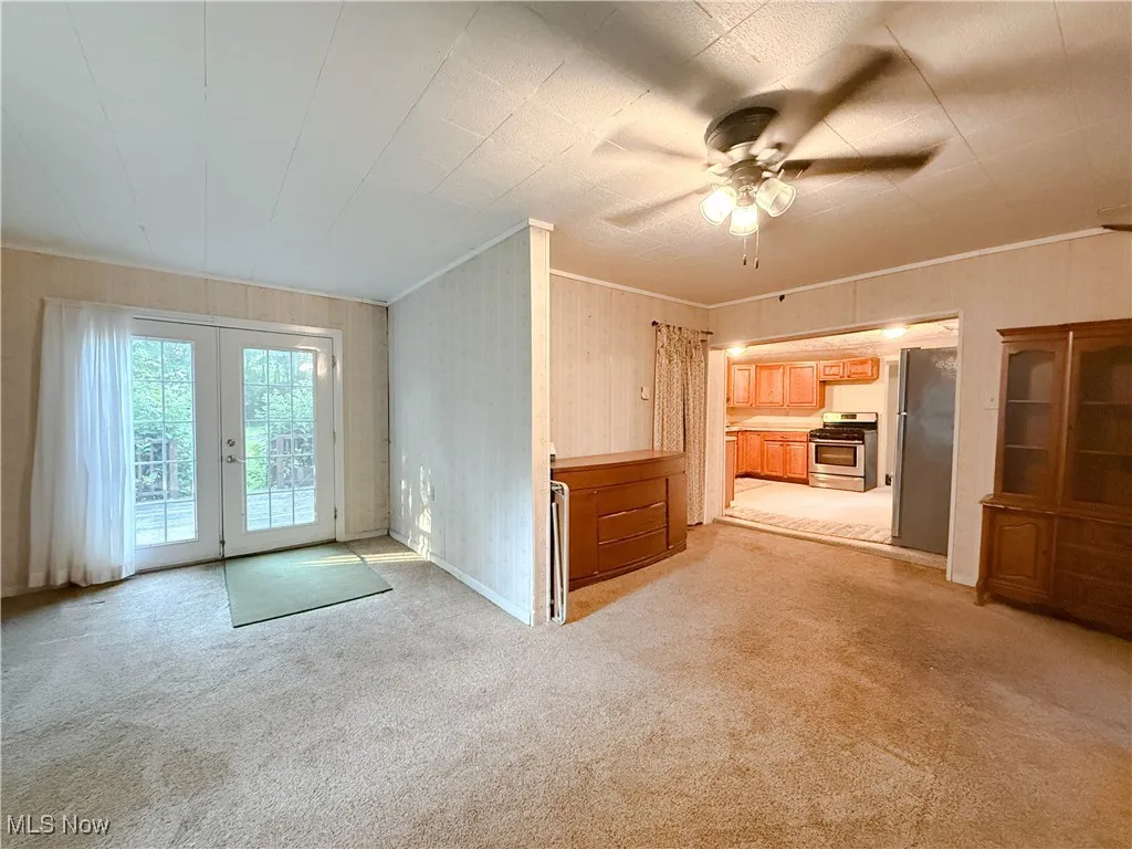 Unfurnished living room with ceiling fan, light carpet, french doors, and ornamental molding