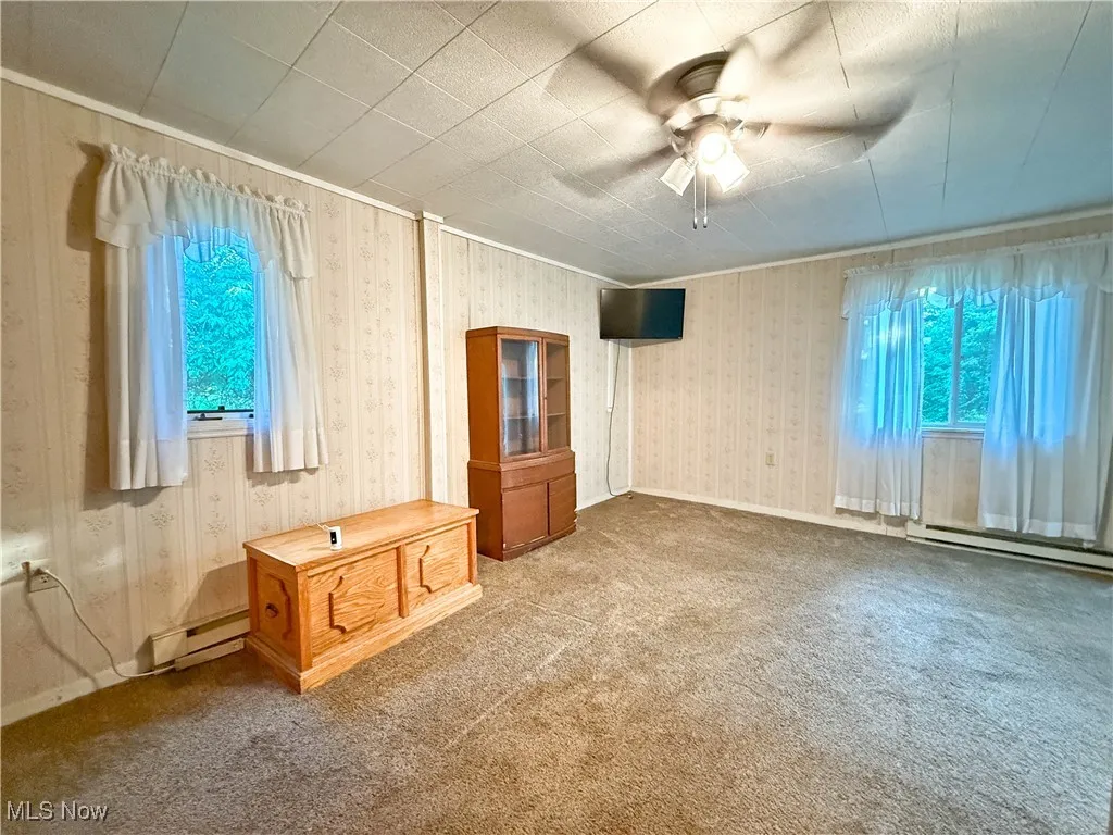 Carpeted spare room with a baseboard radiator, plenty of natural light, a ceiling fan, and wallpapered walls