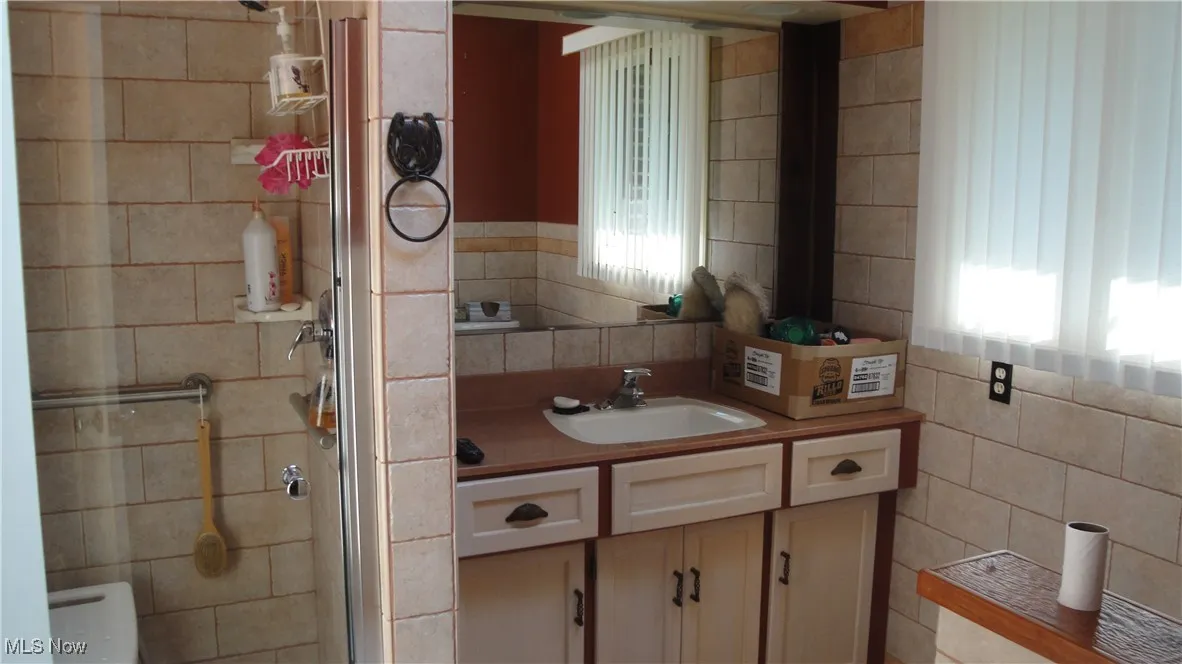 Bathroom with tile walls, a stall shower, and vanity