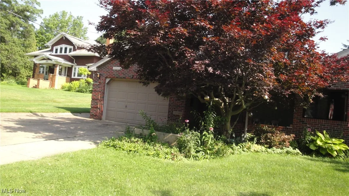 View of property hidden behind natural elements with brick siding, a garage, a front lawn, and concrete driveway