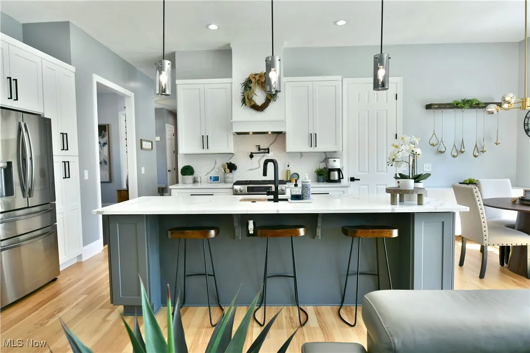 Kitchen featuring stainless steel fridge, white cabinetry, light wood-type flooring, a kitchen breakfast bar, and recessed lighting