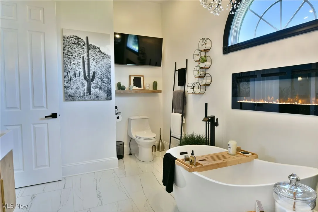 Full bath with a freestanding bath, marble look tiles, and a chandelier