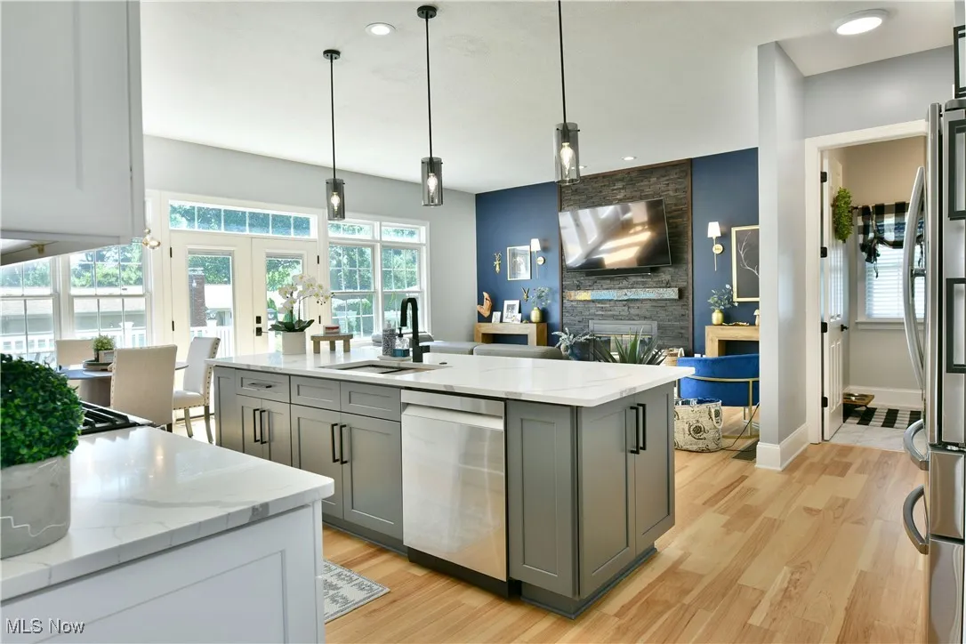 Kitchen featuring stainless steel appliances, gray cabinetry, light wood-style flooring, open floor plan, and light stone counters