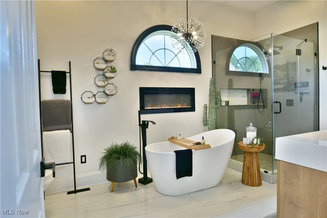 Bathroom with a stall shower, a soaking tub, marble finish flooring, a chandelier, and a glass covered fireplace