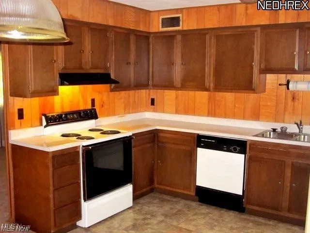 Kitchen featuring white appliances, exhaust hood, light countertops, brown cabinets, and wooden walls
