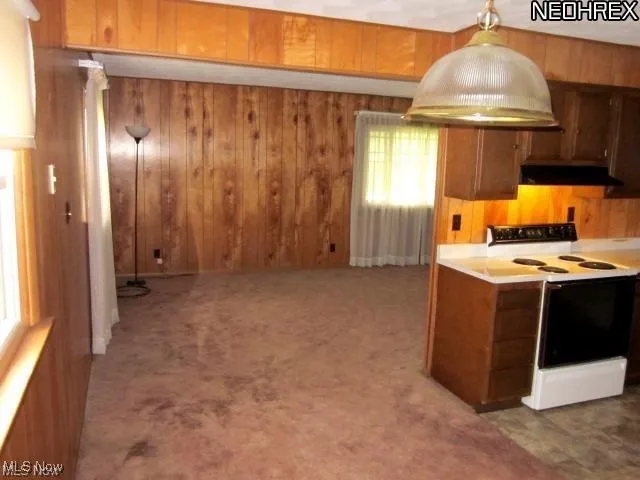 Kitchen featuring white electric range, range hood, wood walls, brown cabinetry, and light countertops