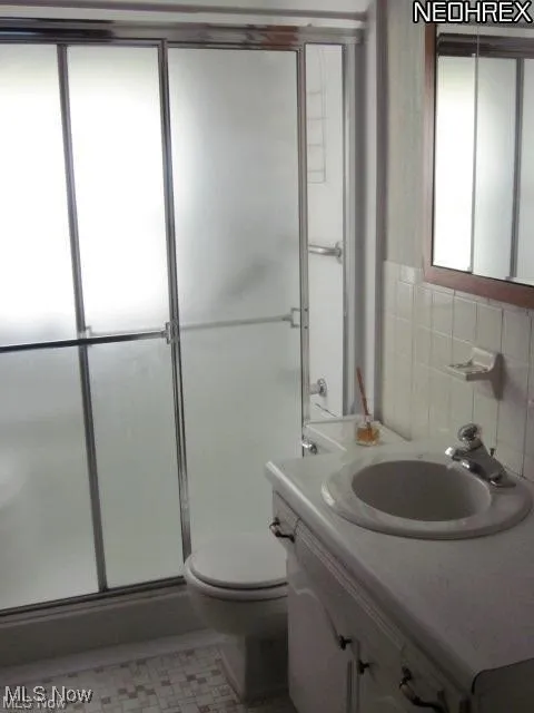 Bathroom featuring a shower stall, vanity, and tile walls