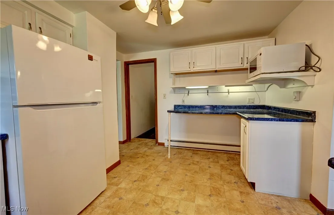 Kitchen with freestanding refrigerator, a baseboard radiator, a ceiling fan, white cabinetry, and dark countertops