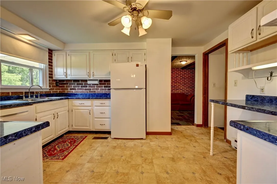 Kitchen with freestanding refrigerator, a ceiling fan, dark countertops, open shelves, and tasteful backsplash