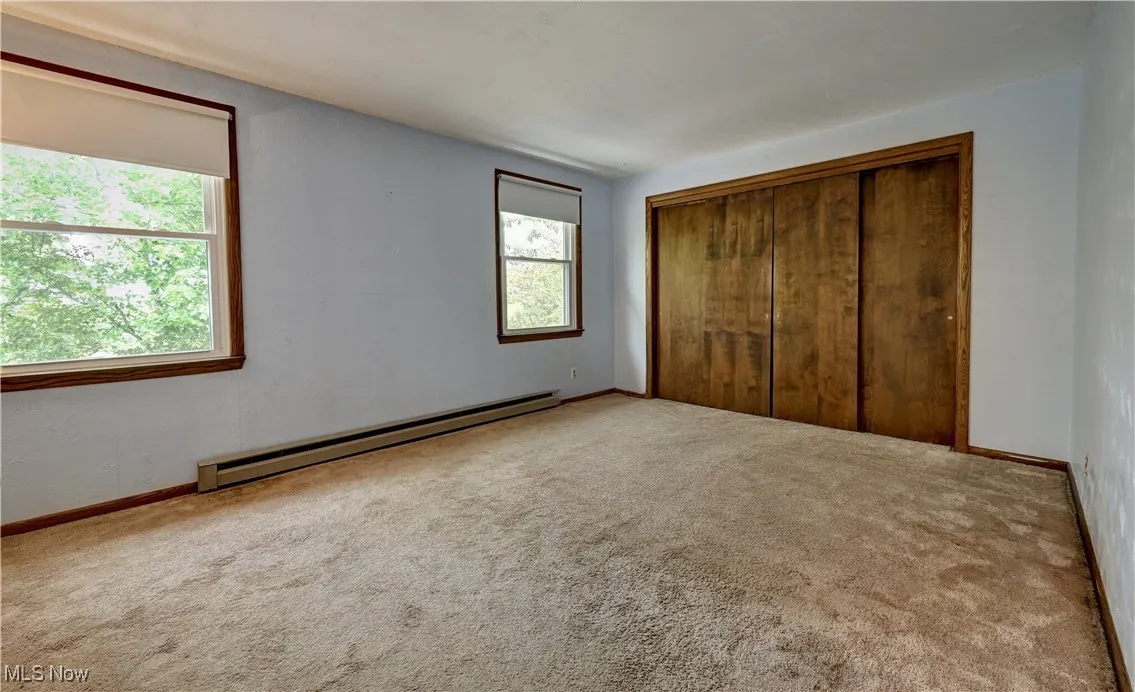 Unfurnished bedroom with a baseboard heating unit, carpet, and a closet