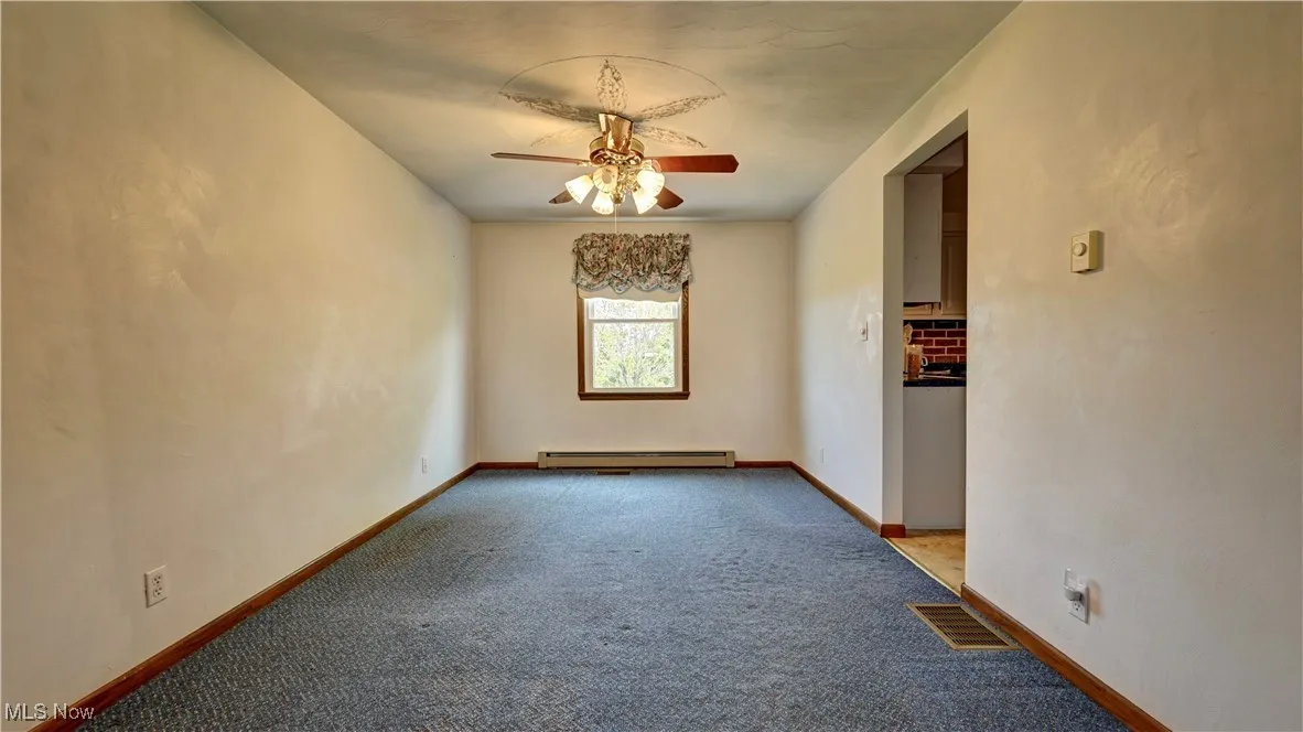 Carpeted empty room featuring baseboard heating and a ceiling fan
