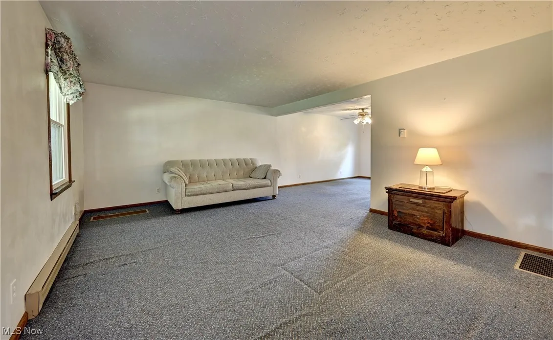 Living room featuring baseboard heating, carpet, and ceiling fan