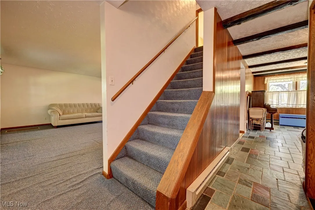 Stairway featuring baseboard heating, stone tile floors, a textured ceiling, and carpet