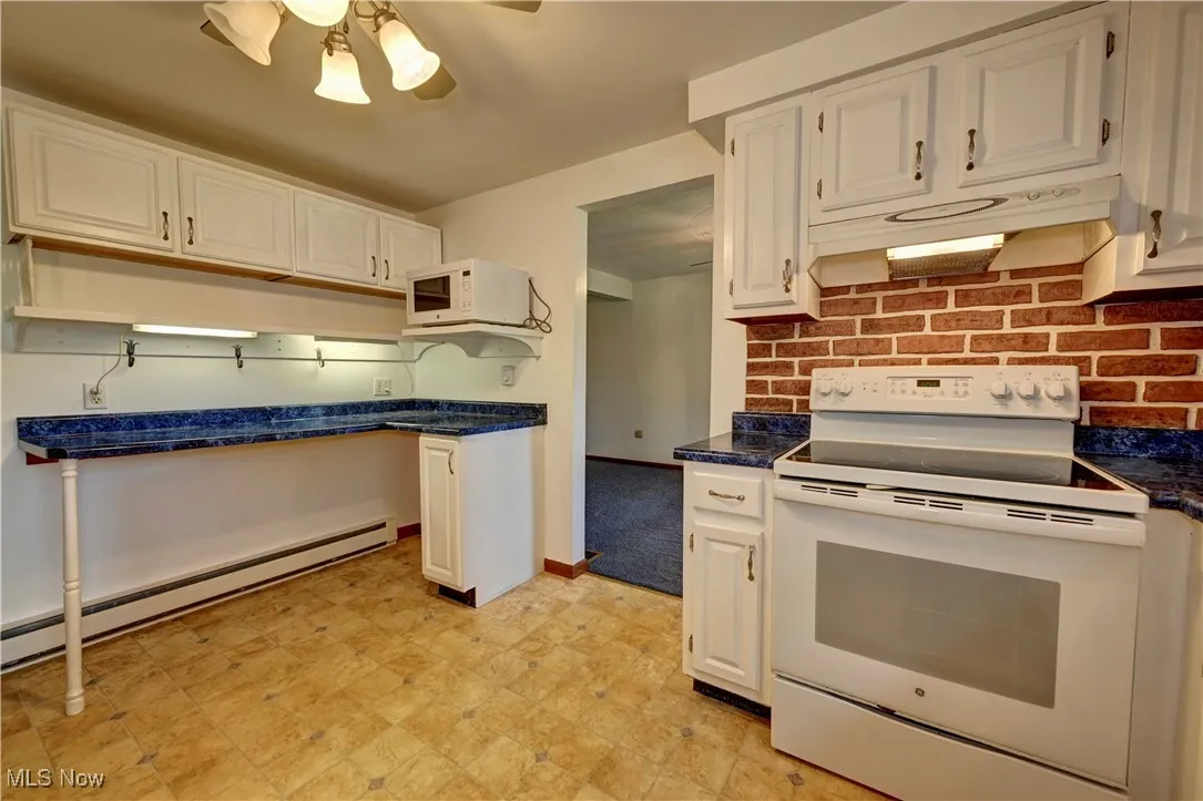 Kitchen with white appliances, under cabinet range hood, a ceiling fan, and dark countertops