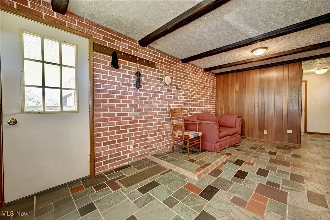 Living area with wooden walls, a textured ceiling, and beamed ceiling