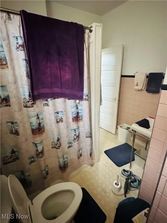Bathroom featuring tile walls, tile patterned floors, a wainscoted wall, and a shower with curtain