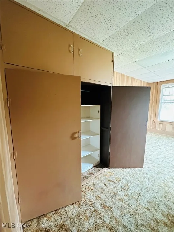 Unfurnished bedroom with carpet flooring, a drop ceiling, and wooden walls