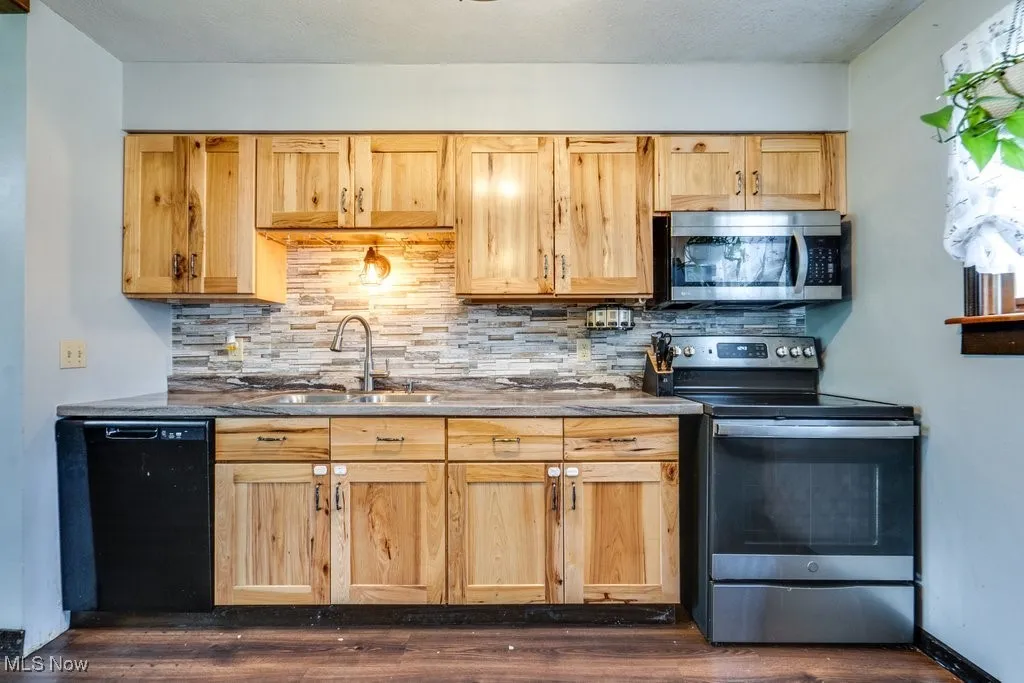 Kitchen featuring stainless steel appliances, backsplash, dark wood-style flooring, and light brown cabinetry