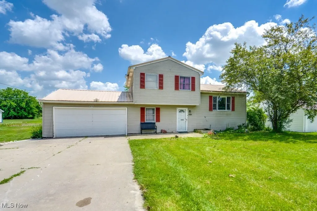 Split level home with driveway, a garage, a front yard, and a metal roof