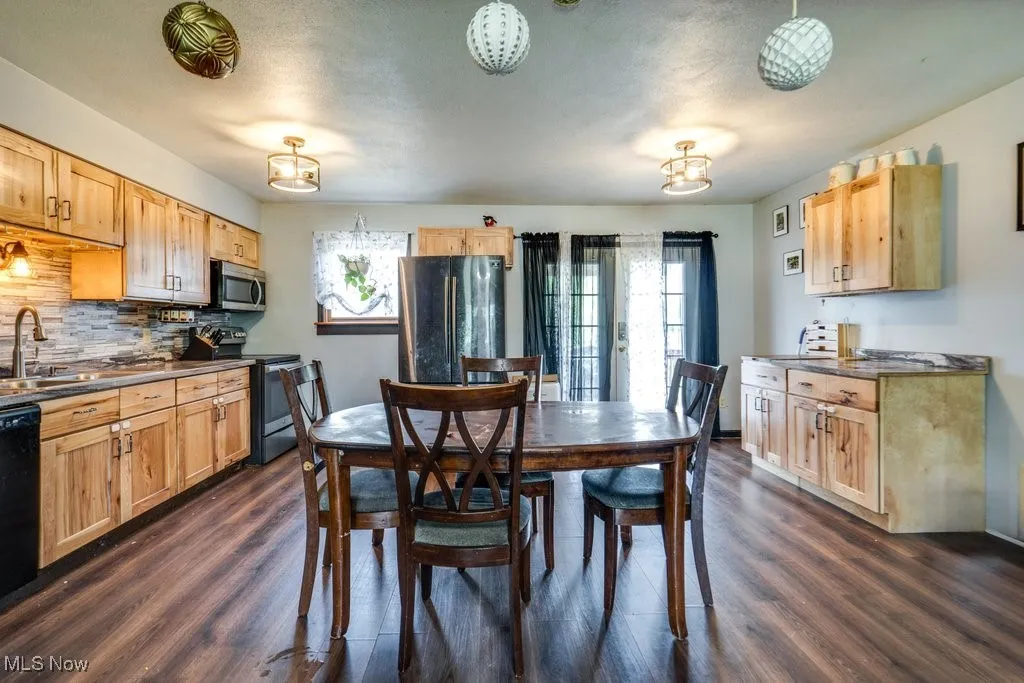 Kitchen with appliances with stainless steel finishes, dark countertops, dark wood-type flooring, and backsplash