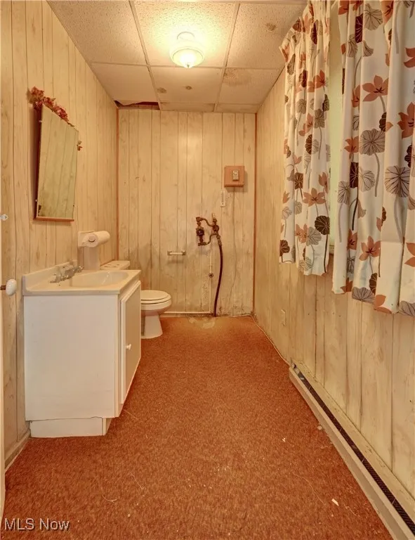 Bathroom featuring baseboard heating, wooden walls, vanity, and a paneled ceiling