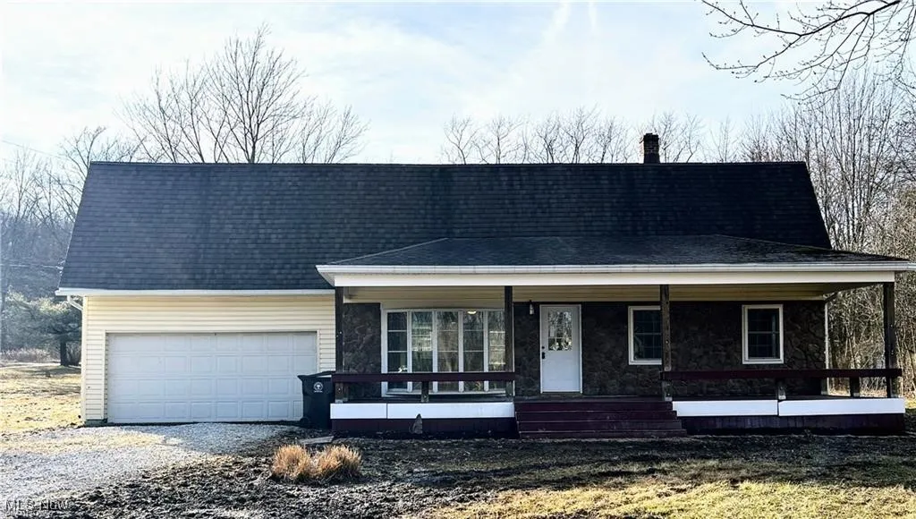View of front of property featuring a porch, an attached garage, gravel driveway, a chimney, and stone siding