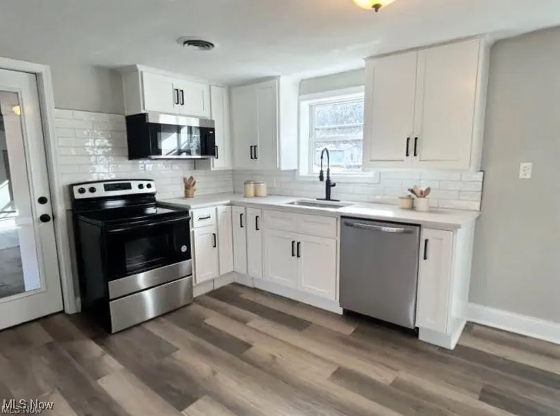Kitchen featuring appliances with stainless steel finishes, white cabinetry, light countertops, tasteful backsplash, and dark wood finished floors