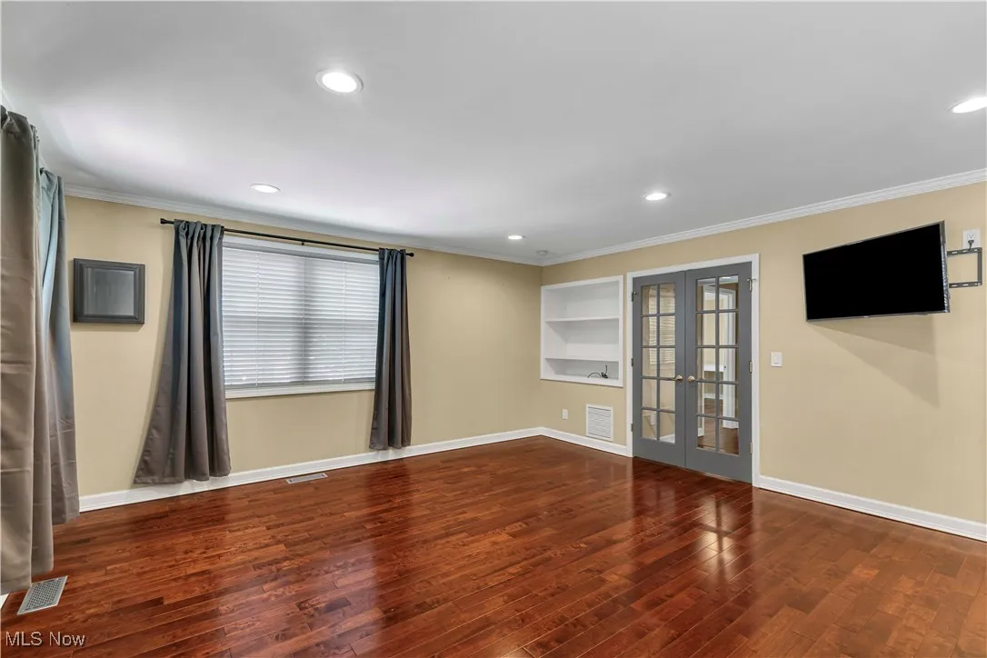 Spacious primary suite on second floor featuring french doors, cherry wood style flooring, custom built-ins, mounted TV and recessed lighting.