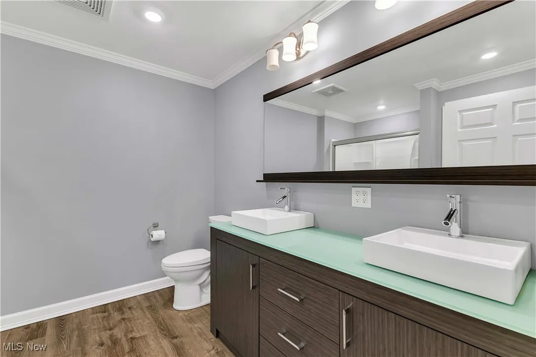Full bathroom with wood finished floors, double vanity, a shower with shower door, crown molding, and recessed lighting