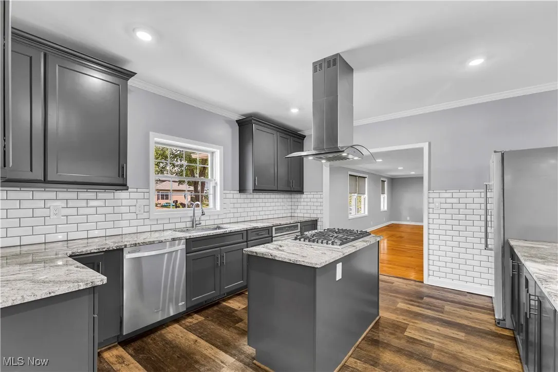 Kitchen featuring modern charcoal gray cabinetry, stainless steel appliances, island range hood, light granite countertops, multi-toned vinyl flooring and tiled backsplash