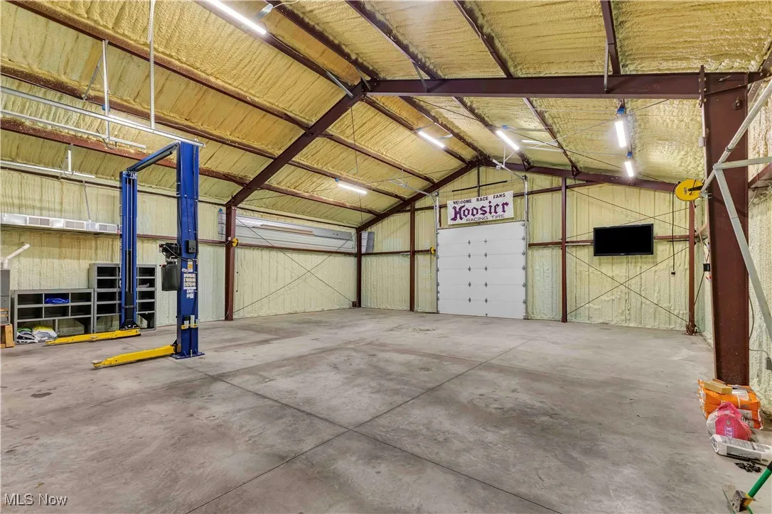 Large outbuilding with concrete floor, overhead lighting and has a door that leads to the backyard.