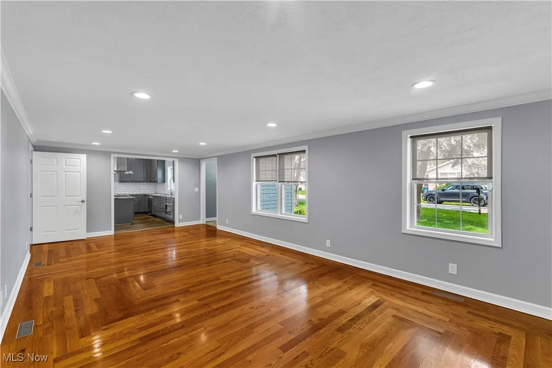 Spacious living room with hardwood floors, recessed lighting, large front windows, white baseboards and crown molding.
