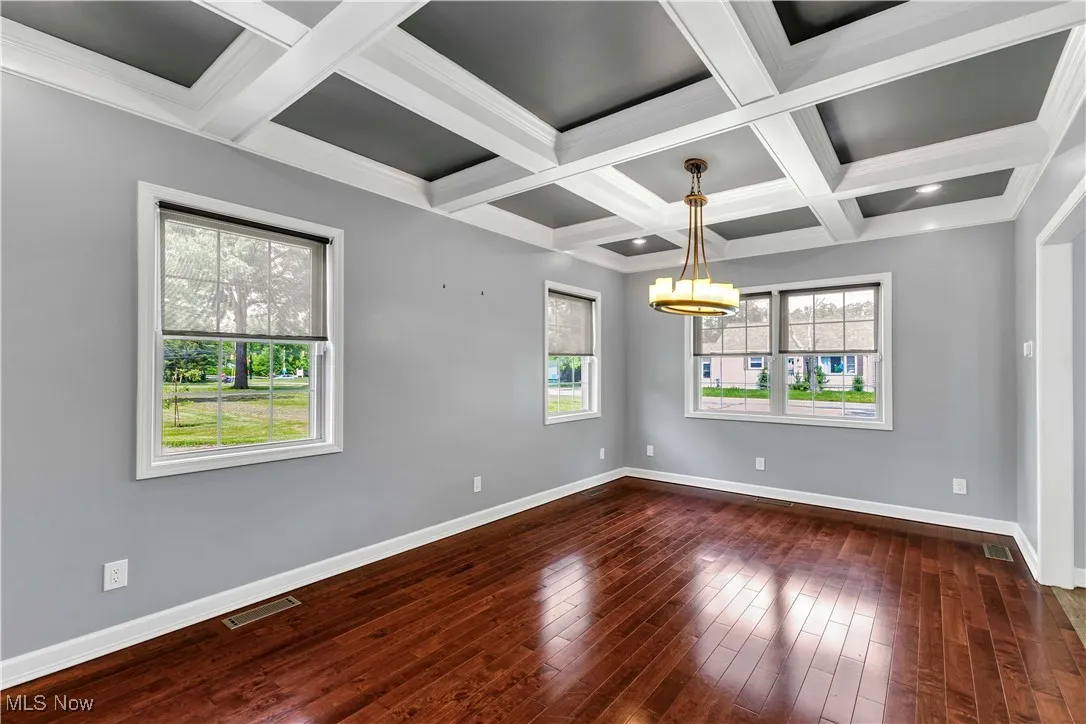 Formal dining room featuring a chandelier, dark wood-type flooring, coffered ceiling, and ornamental molding
