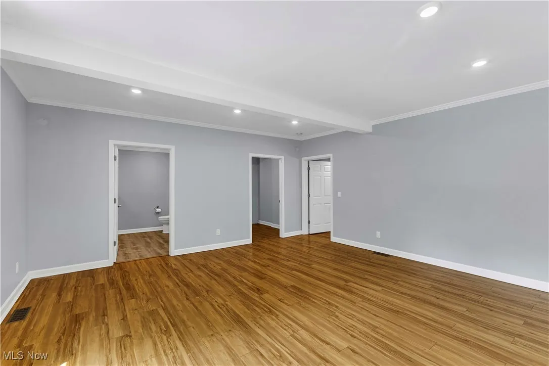 First floor primary suite featuring ornamental molding, wood finished floors, recessed lighting, and beamed ceiling.