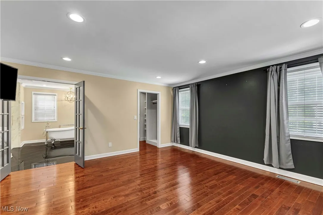 Spacious primary suite on second floor featuring french doors, cherry wood style flooring, custom built-ins, mounted TV and recessed lighting.
