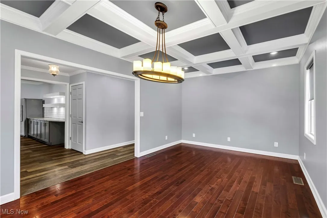 Formal dining room featuring a chandelier, dark wood-type flooring, coffered ceiling, and ornamental molding