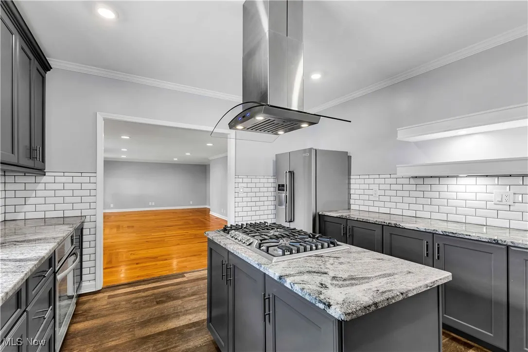 Kitchen featuring modern charcoal gray cabinetry, stainless steel appliances, island range hood, light granite countertops, multi-toned vinyl flooring and tiled backsplash