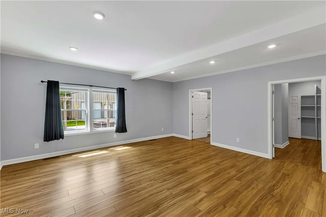 First floor primary suite featuring ornamental molding, wood finished floors, recessed lighting, and beamed ceiling.