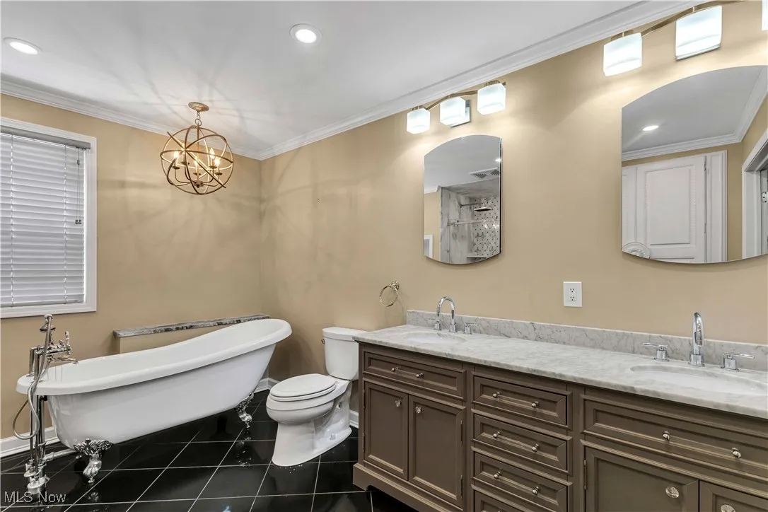 Primary bathroom on second floor featuring sleek black tile floors, marble double vanities, clawfoot soaking tub, a dual rainfall tile shower and a chandelier.