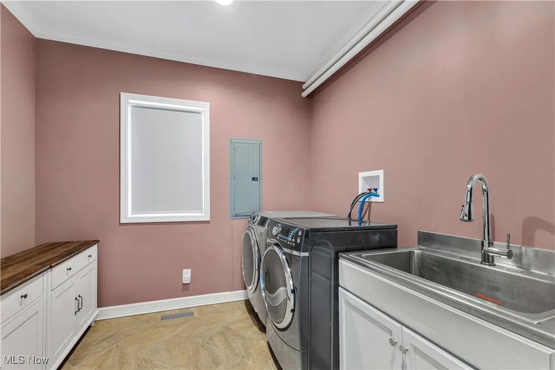 Laundry/mudroom featuring storage/folding cabinet, electric panel, separate washer and dryer, utility tub, tankless water heater and storage closet.