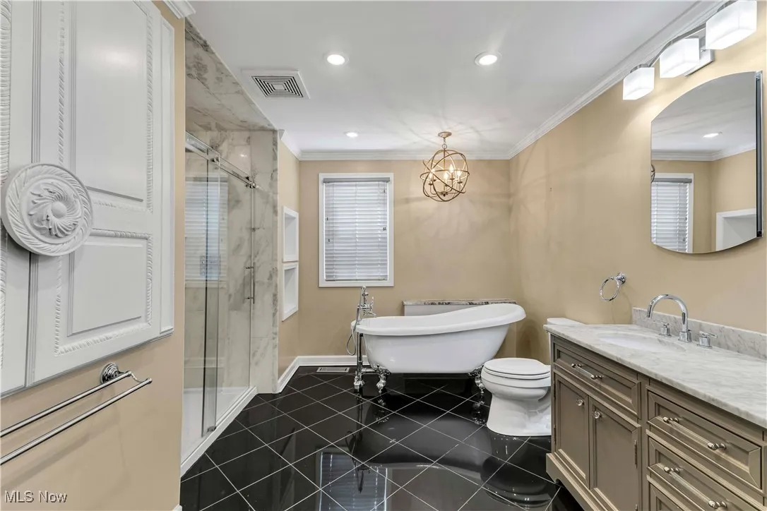 Primary bathroom on second floor featuring sleek black tile floors, marble double vanities, clawfoot soaking tub, a dual rainfall tile shower and a chandelier.