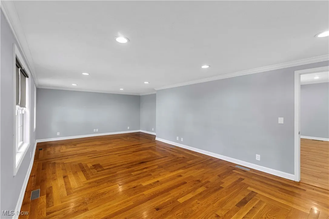 Spacious living room with hardwood floors, recessed lighting, large front windows, white baseboards and crown molding.