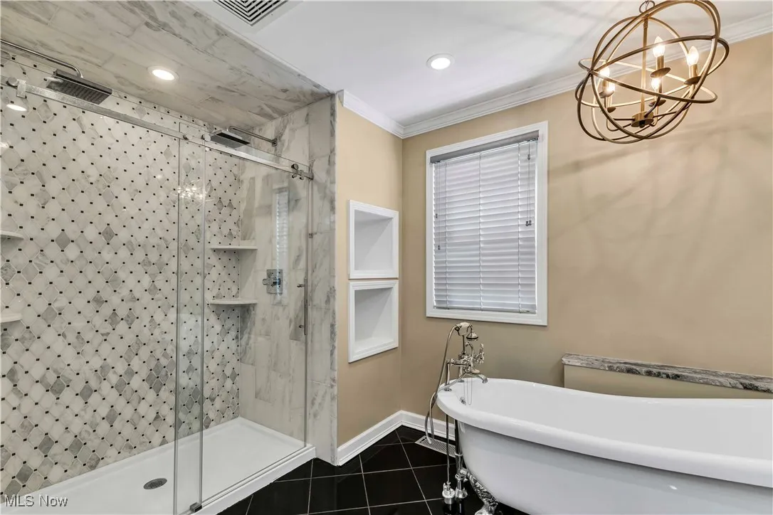 Primary bathroom on second floor featuring sleek black tile floors, marble double vanities, clawfoot soaking tub, a dual rainfall tile shower and a chandelier.