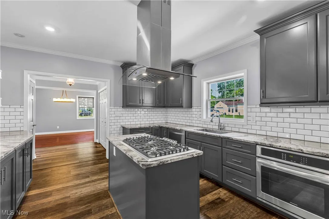 Kitchen featuring modern charcoal gray cabinetry, stainless steel appliances, island range hood, light granite countertops, multi-toned vinyl flooring and tiled backsplash