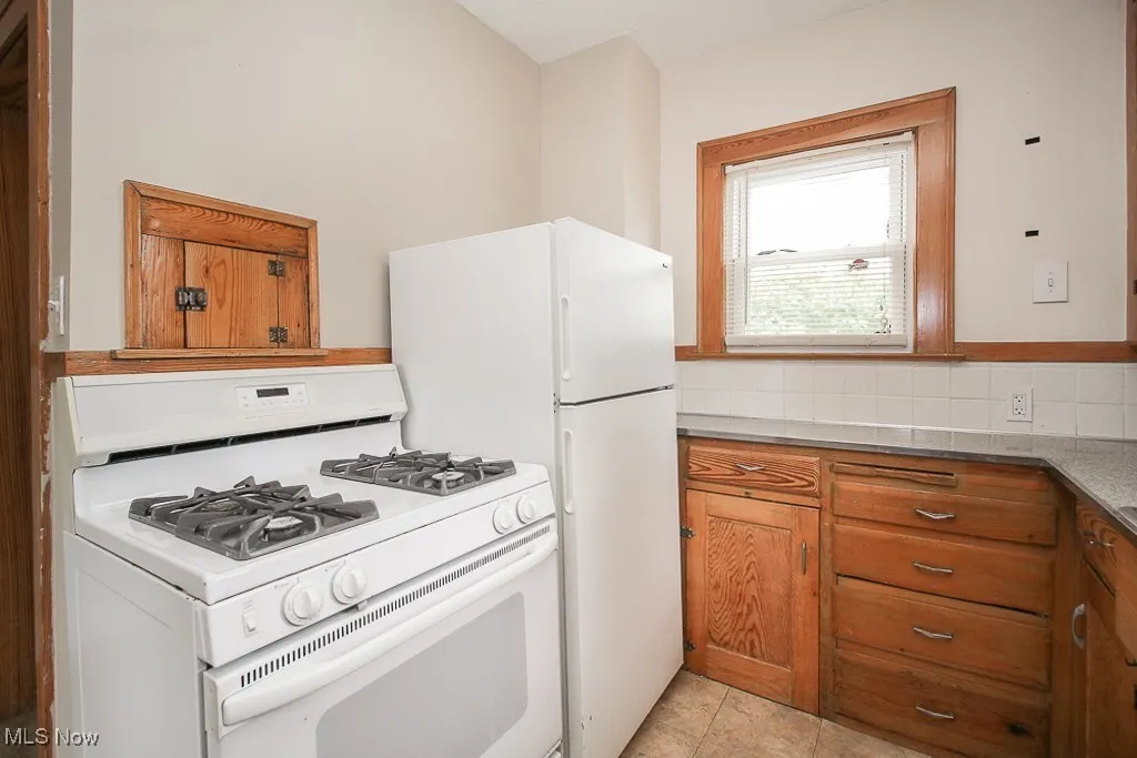Kitchen featuring white range with gas cooktop, brown cabinets, and light tile patterned flooring